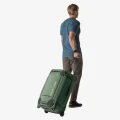 Eagle Creek Gear Warrior XE 27 – Jungle Green, ujęcie lifestyle: prowadzenie walizki na kółkach