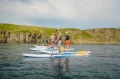 Pompowane deski SUP Gladiator Elite - duża grupa osób na wodzie obok klifów_half.webp