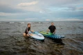 kobieta i mężczyzna z deskami SUP Gladiator wychodzą z morza na kamienistą plażę.webp