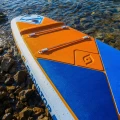 Gladiator Elite 12'6T – rufa deski SUP na kamienistym brzegu, pomarańczowy deckpad i linki bagażowe