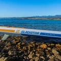 Gladiator Elite 12'6LT – detal burty z napisem Gladiator, deska SUP na kamienistym brzegu