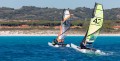 MiniCat 420 – dwa katamarany na wodzie (catamaran); zielony i pomarańczowy żagiel.