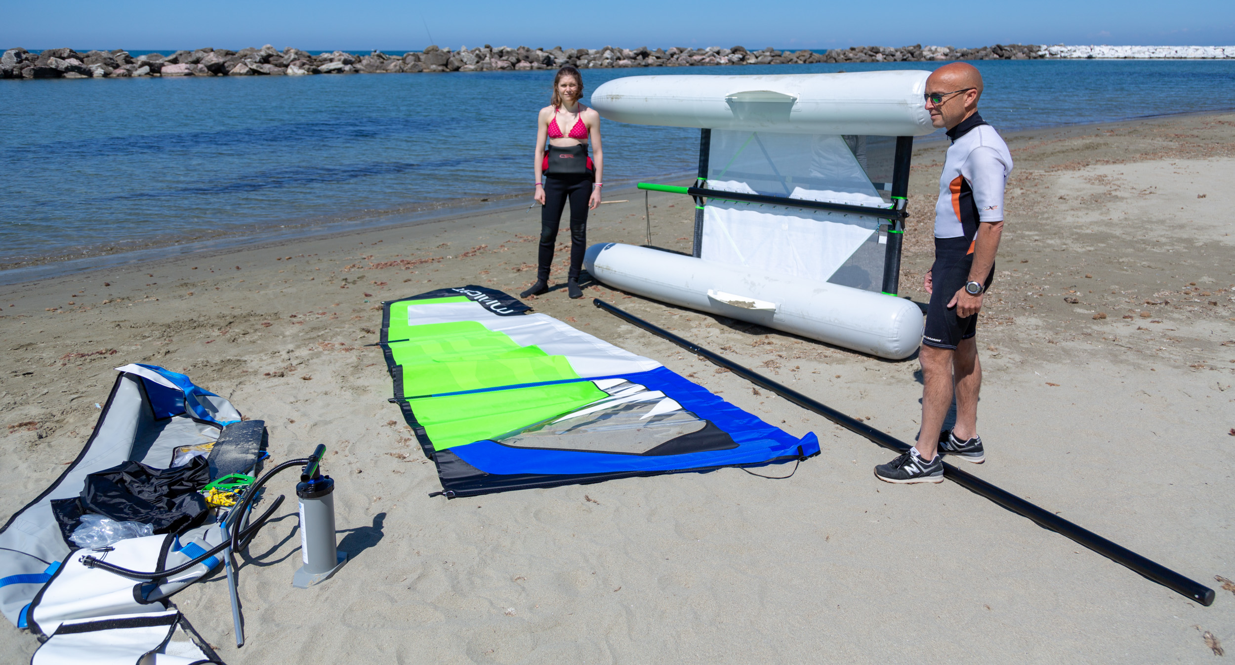 Widok ogólny  zmontażu Minicat Guppy na plaży - torba, żagiel i katamaran na boku.