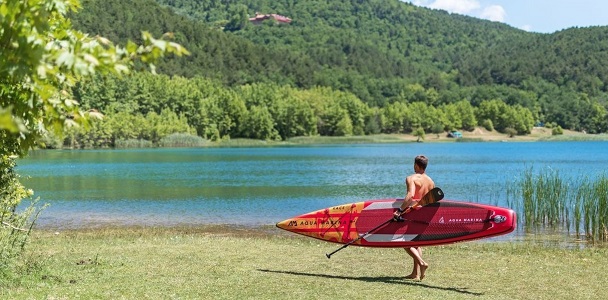 Osoba z deską SUP race idzie w stronę jeziora – paddleboarding dla zaawansowanych