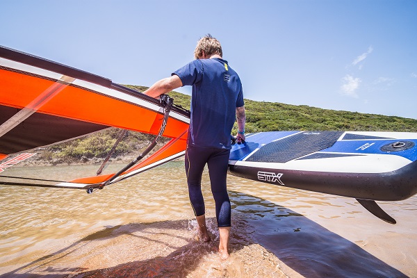 Osoba niesie zestaw do windsurfingu - deskę pompowaną windsup STX z pędnikiem